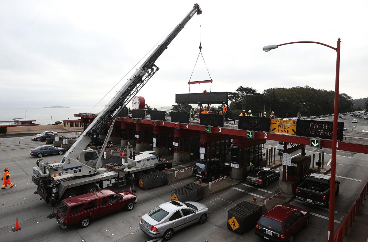 Workers use a crane to lower a new sign onto the top of the Golden Gate Bridge toll plaza. Starting Wednesday, the bridge will no longer have toll-booth operators.
