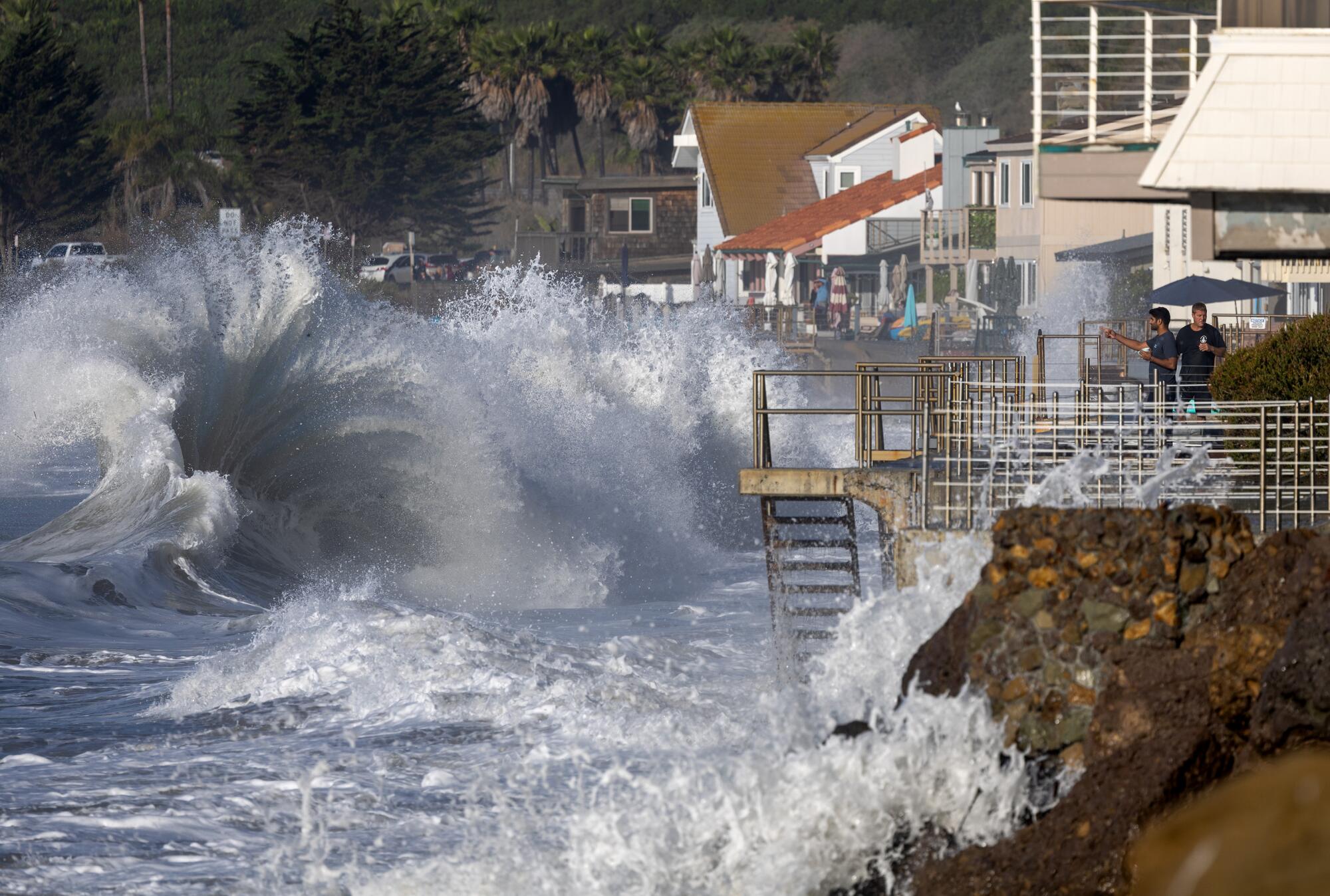 Men watch from a balcony as huge waves crash on the shore.