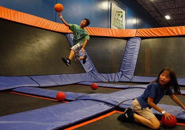 At Sky Zone in Anaheim this week, Micah Kim, 10, jumps high off a trampoline to throw a dodge ball as Lauren Lee, 8, grabs a ball. There are an estimated 100-plus indoor trampoline parks in the United States.