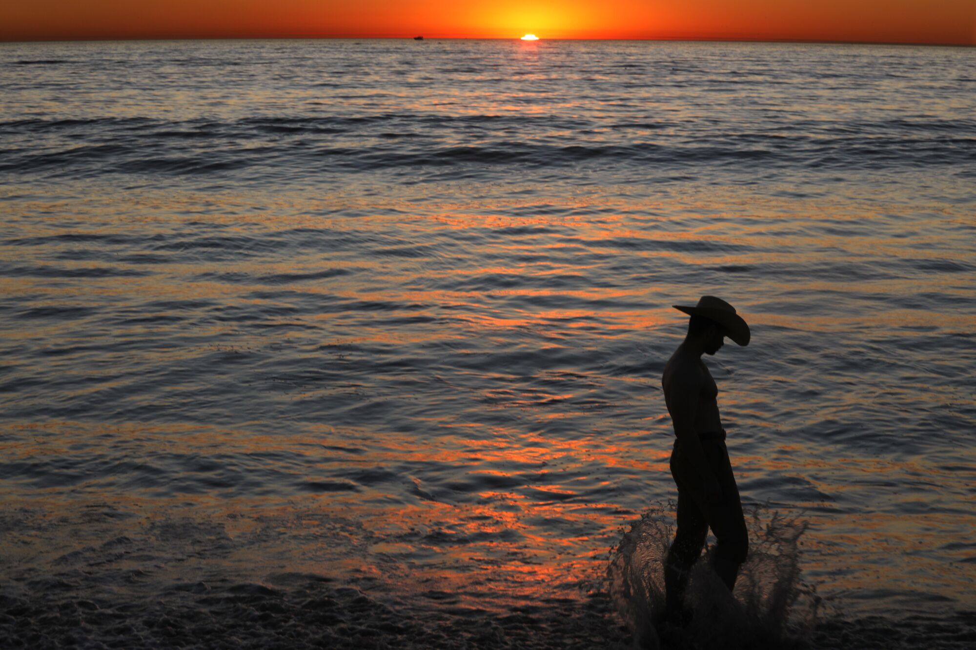 Michael Sparks in silhouette with a cowboy hat on as the sun sets on the water behind him.