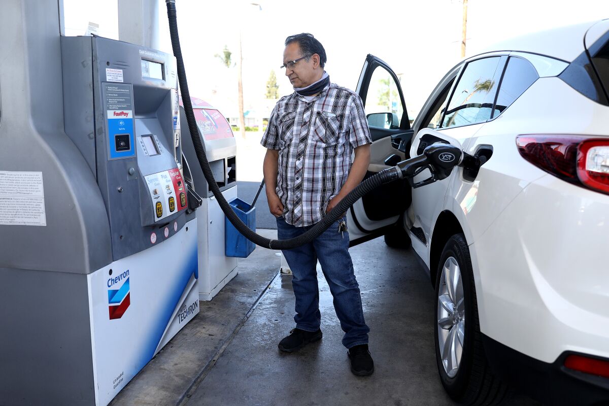 A man stands with hands in his pockets watching a gas pump as his car is filled with gas.