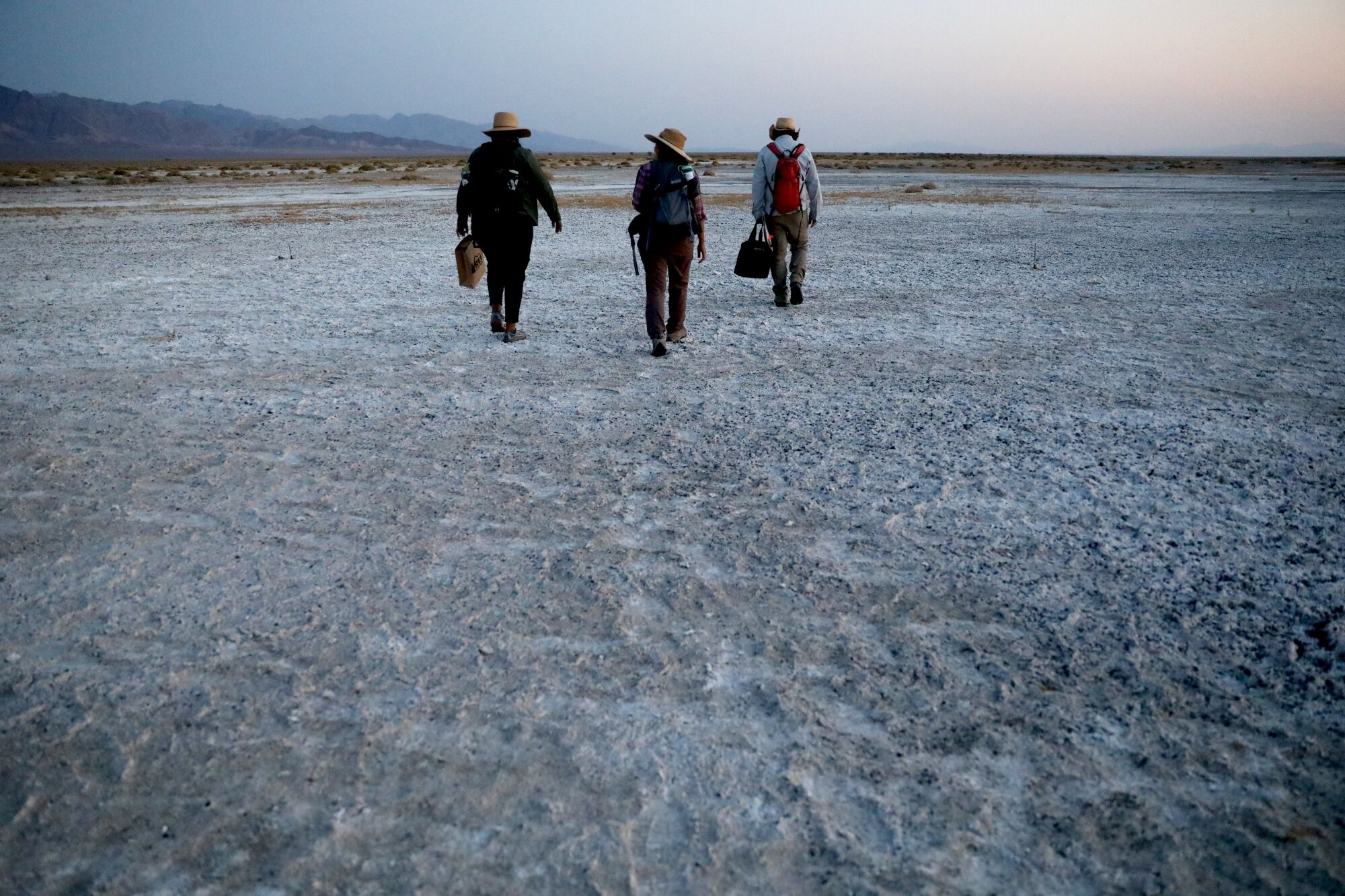 Three people trudge over a craggy desert plain