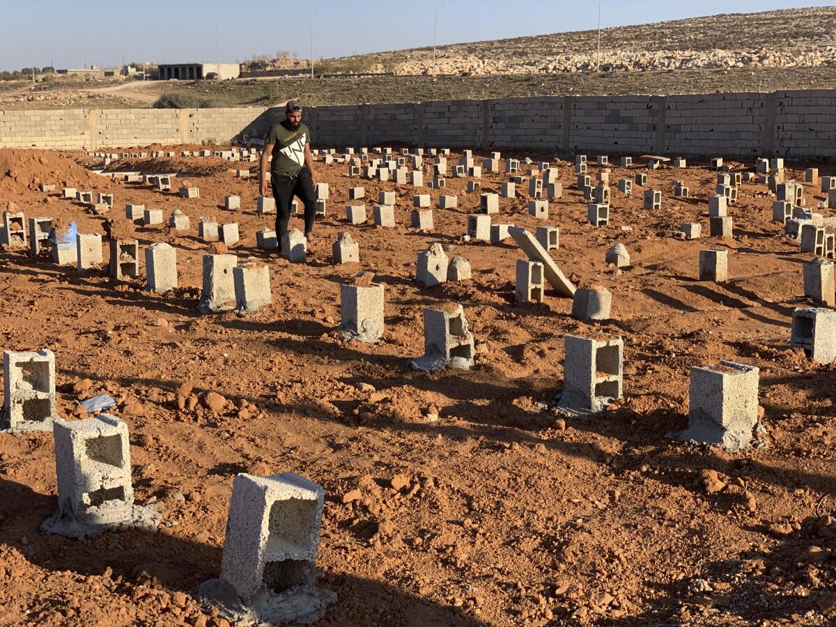 A man walks by rows of graves marked with cinder blocks