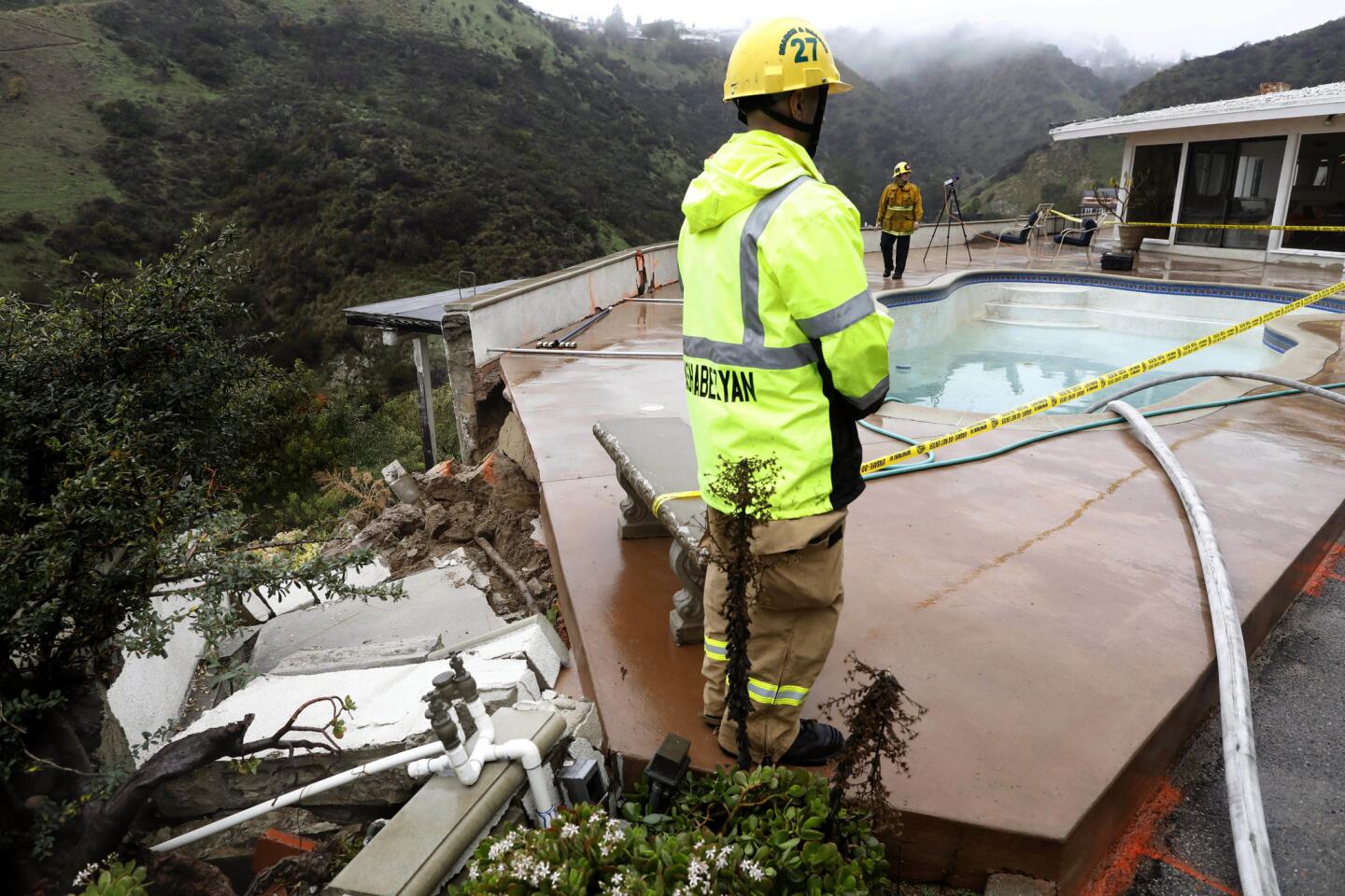 L.A. firefighters oversee drainage of a pool in the yard of a Hollywood Hills home. The pool was compromised as soil shifted during the recent rains.