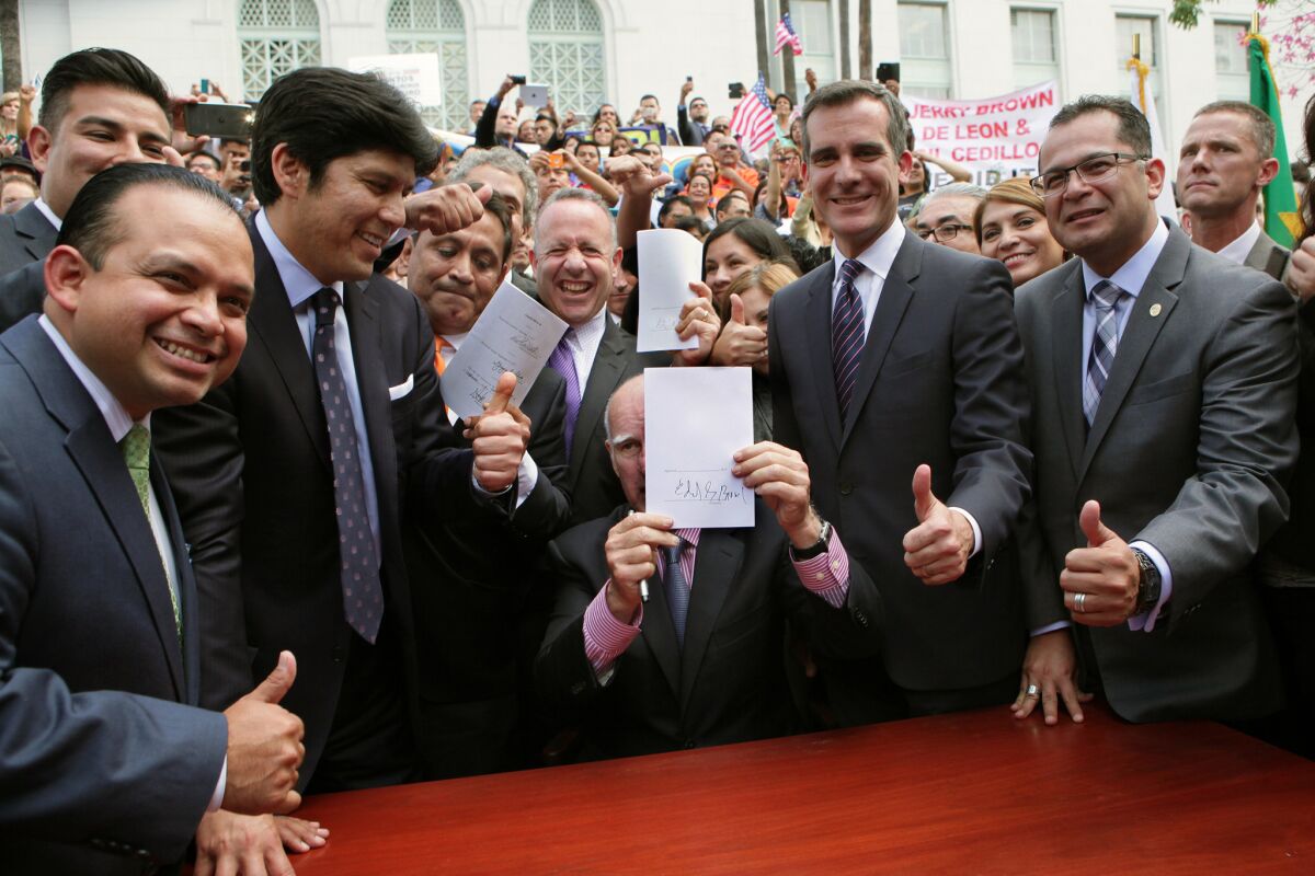 From left, Assemblyman Luis Alejo, state Sen. Ricardo Lara (partially visible), Sen. Kevin de León, Los Angeles City Councilman Gil Cedillo, Senate leader Darrell Steinberg, Mayor Eric Garcetti and Assemblyman V. Manuel Perez give a thumbs-up as Gov. Jerry Brown holds up a signed bill that will allow immigrants lacking legal immigration status to obtain California driver's licenses.
