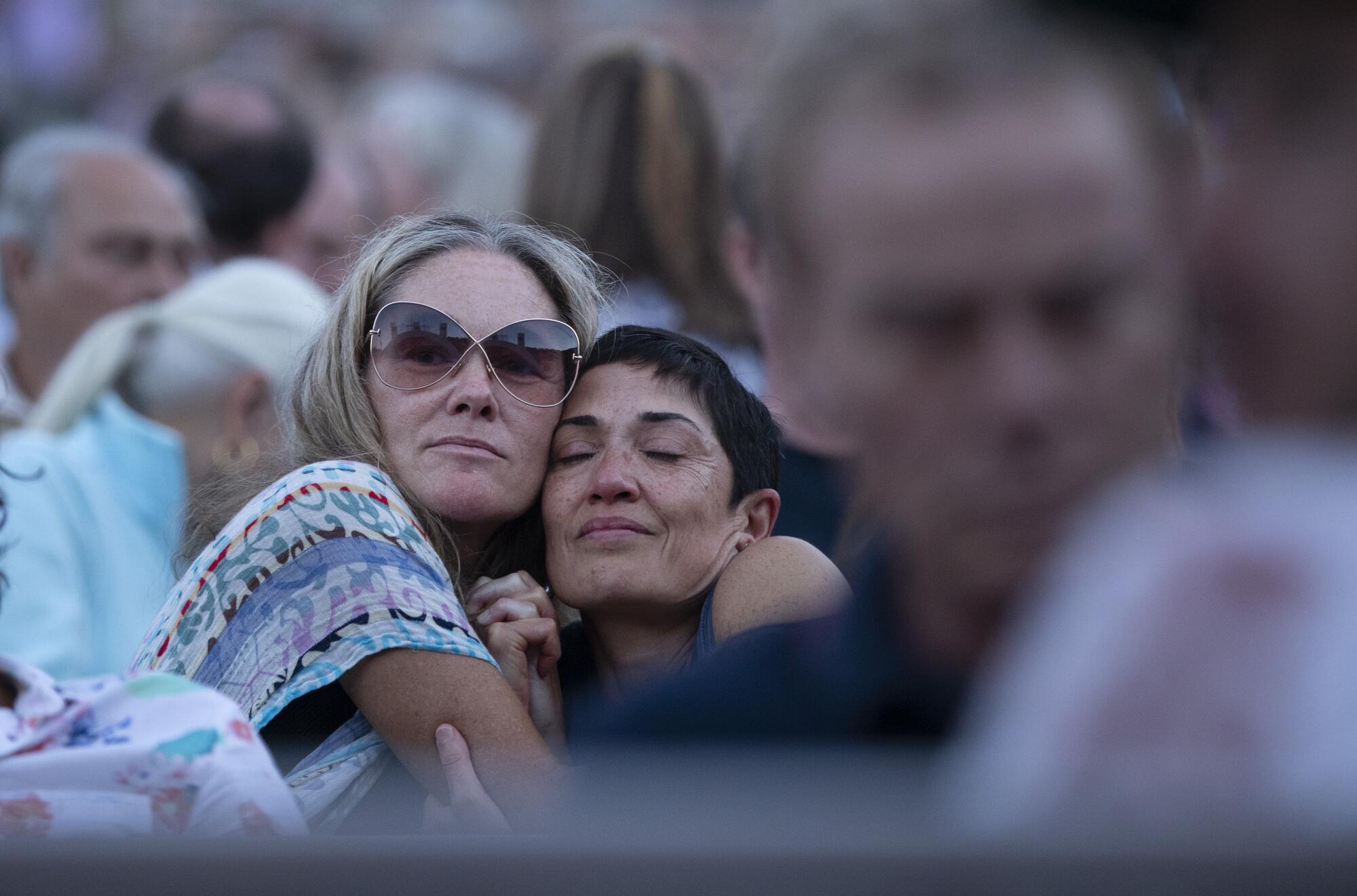 Amid a seated crowd, two women hug.