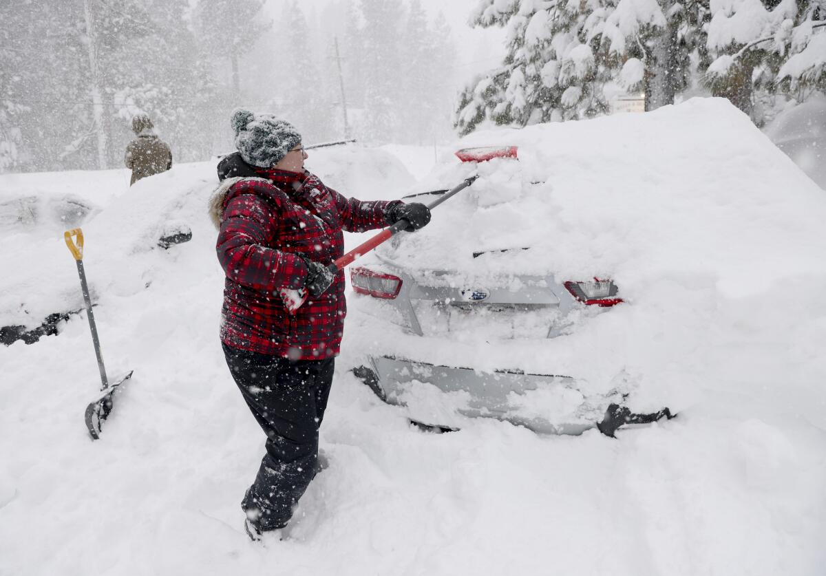 A woman uses a brush to clear heavy snow off her car.