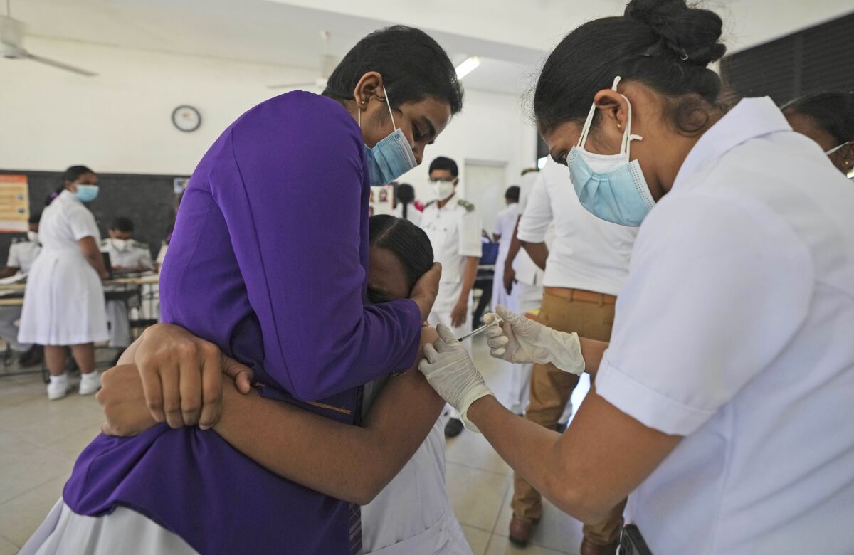 A Sri Lankan school student reacts holding another student as she receives her first COVID-19 vaccine from a health worker in Colombo, Sri Lanka, Friday, Jan. 7, 2022. Sri Lankan health authorities starting to inoculate the children in the age group of 12 to 15 in it’s latest effort to contain the spreading of COVID-19 as the island nation’s top medical specialists warned of a massive wave of infection driven by the Omicron variant in the coming weeks. (AP Photo/Eranga Jayawardena)