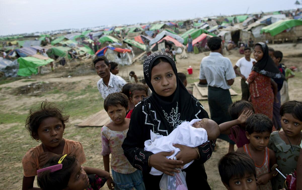 An internally displaced Rohingya woman holds her newborn baby surrounded by children in the foreground of makeshift tents at a camp for Rohingya people in Sittwe, Myanmar. Authorities in Myanmar's western Rakhine state have imposed a two-child limit for Muslim Rohingya families, a policy that does not apply to Buddhists in the area and comes amid accusations of ethnic cleansing in the aftermath of sectarian violence.