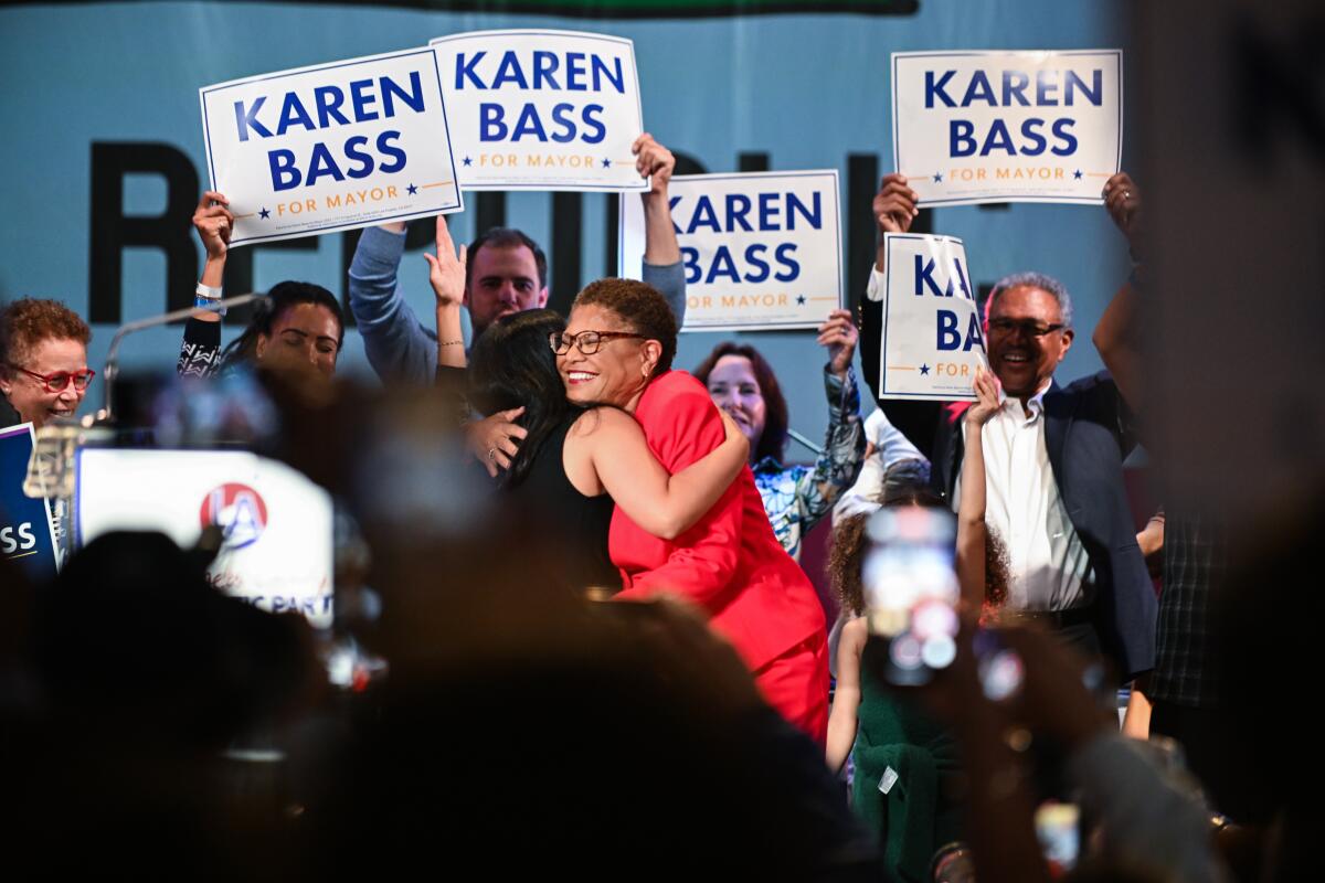 Two women hug as others hold up "Karen Bass" signs. 