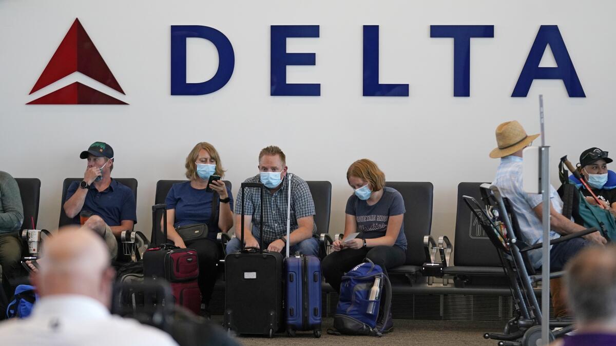 People sit under Delta sign at Salt Lake City International Airport on July 1, 2021, in Salt Lake City. Air travel in the United States hit another pandemic-era record over the weekend as vacationers jammed airports, but shares of airlines, cruise lines, hotels and almost anything else related to travel are tumbling on growing concerns about highly contagious variants of coronavirus. (AP Photo/Rick Bowmer)