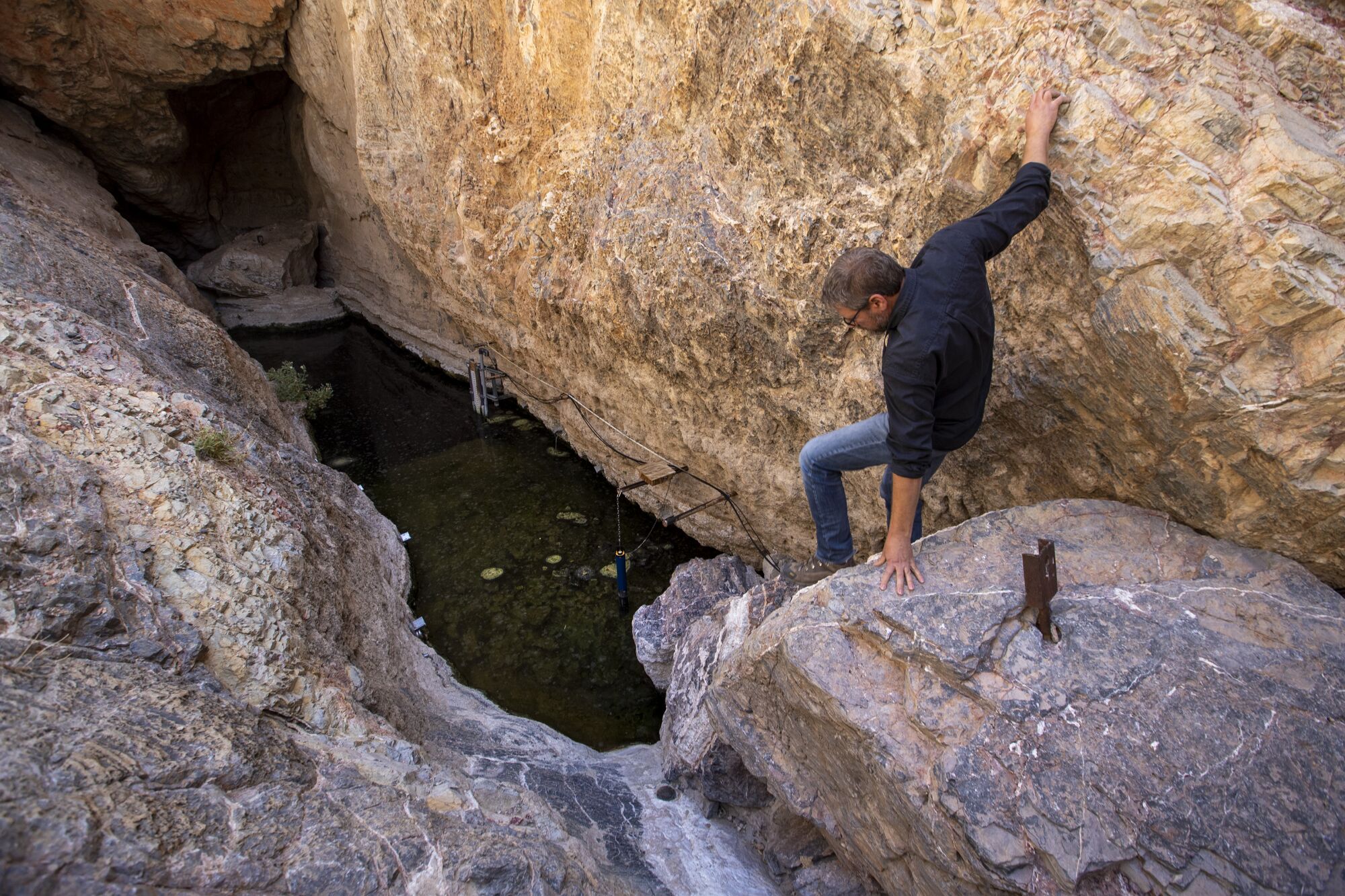 A man climbs down off a rock next to a small pool of water 