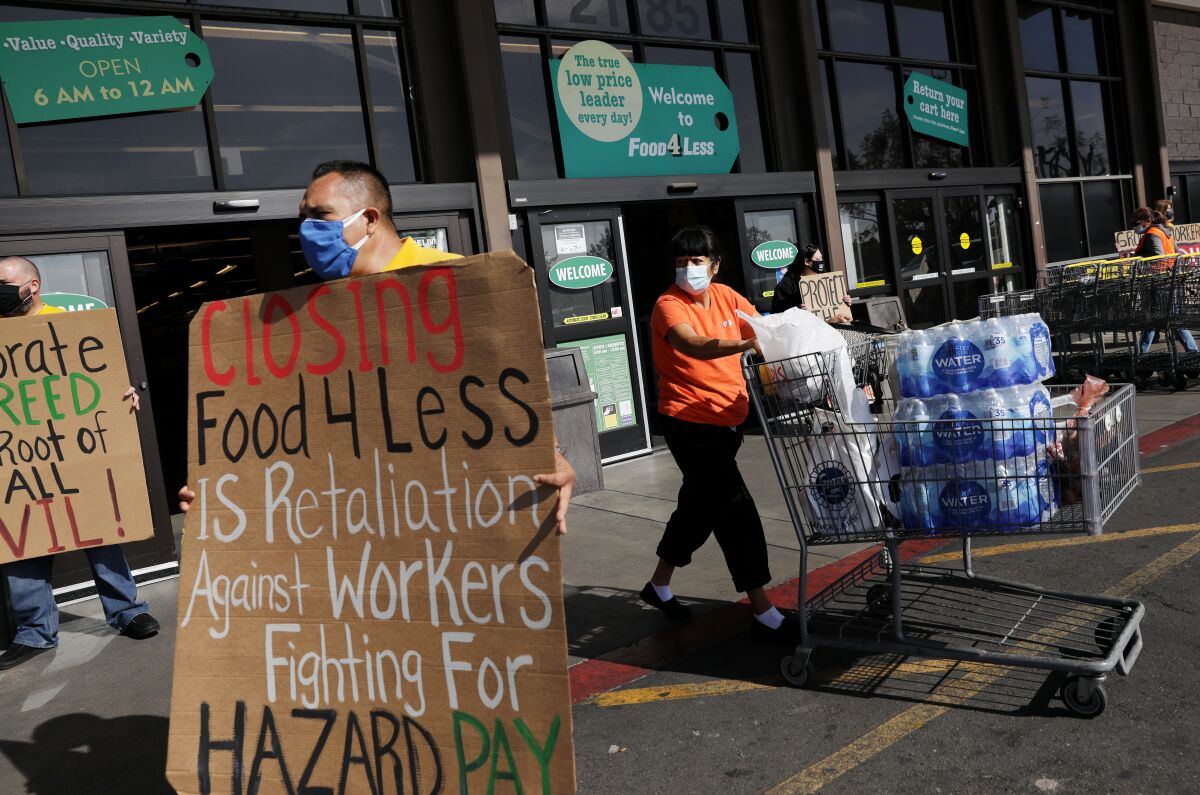 A man holds a sign that reads "Closing Food 4 Less is retaliation against workers fighting for hazard pay."