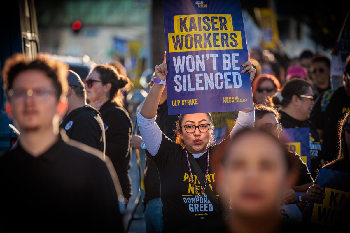Picketers. One holds a sign reading "Kaiser workers won't be silenced."