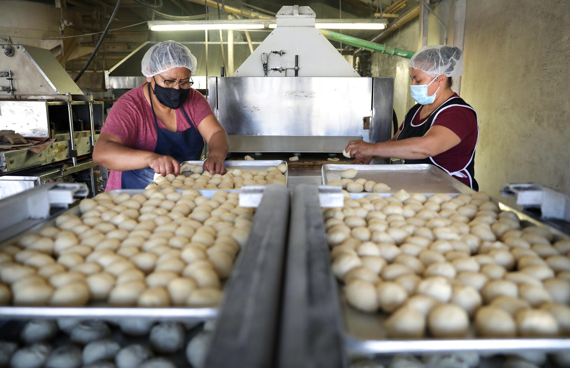 Two workers stand next to balls of dough on a machine