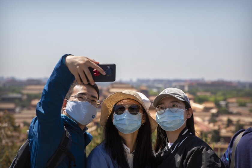 Visitors wearing face masks pose for a selfie at a viewing area overlooking the Forbidden City at a public park in Beijing, Saturday, May 1, 2021. Chinese tourists are expected to make a total of 18.3 million railway passenger trips on the first day of the country's five-day holiday for international labor day, according to an estimate by the state railway group, as tourists rush to travel domestically after the coronavirus has been brought under control in China.(AP Photo/Mark Schiefelbein)