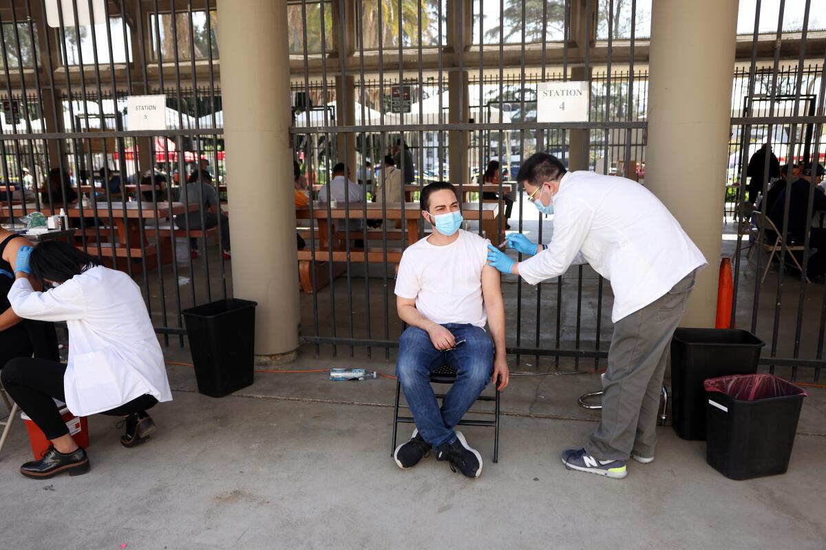 A healthcare worker administers a shot to a man seated in a folding chair at an outdoor clinic.