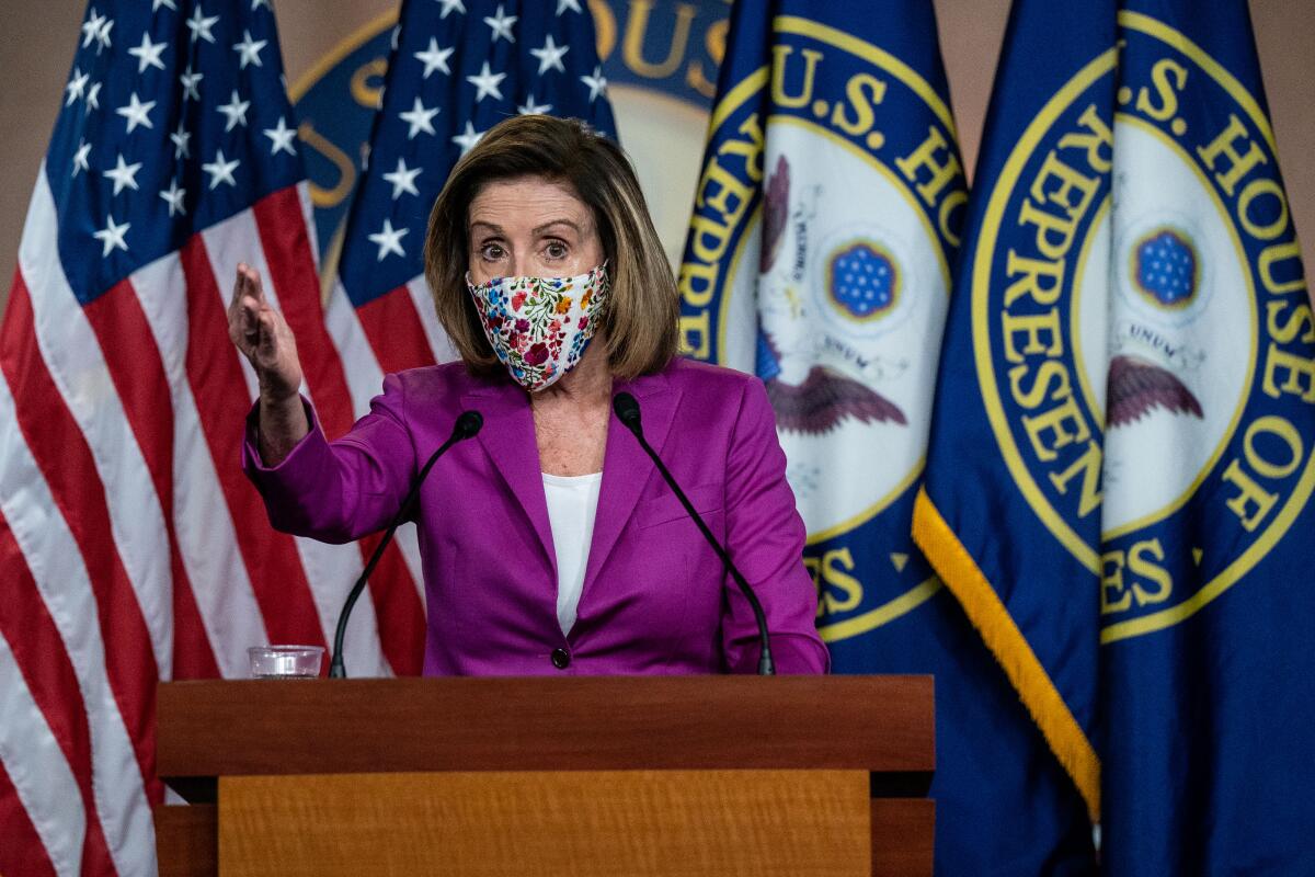 Nancy Pelosi, in mask, gestures as she stands at a podium and speaks into microphones.