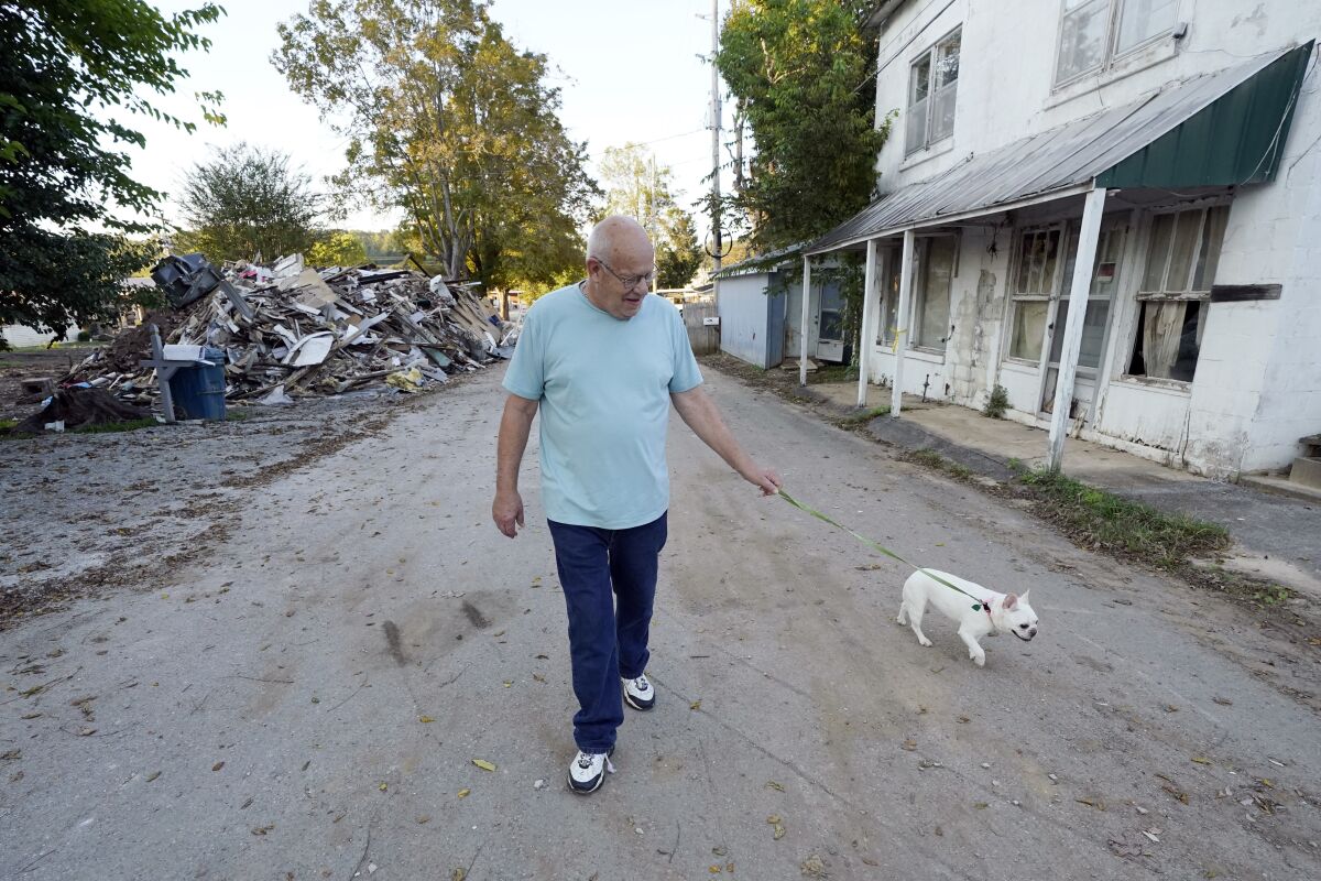 Tommy Goodwin walks his dog, Tasha, down a street lined with flood-damaged buildings and piles of debris Sept. 27, 2021, in Waverly, Tenn. After a devastating flood hit Aug. 21, the town of just over 4,000 people faces a dilemma. More than 500 homes and 50 businesses were damaged. That will likely result in massive revenue losses while the city spends millions on cleanup and repairs. If those homes and businesses don't return, the town could die a lingering death. But if they build back along the creek, they could be risking another disaster. (AP Photo/Mark Humphrey)