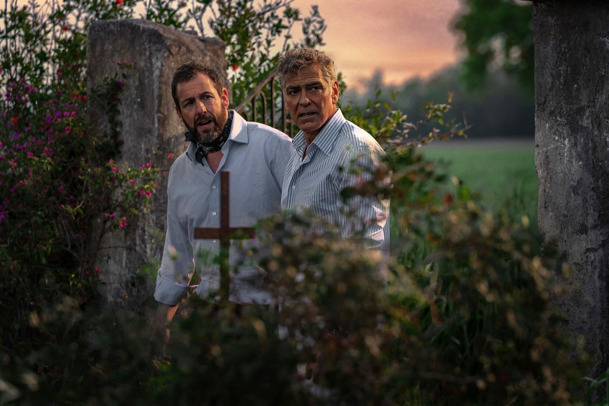Two men stand outside a gated garden.