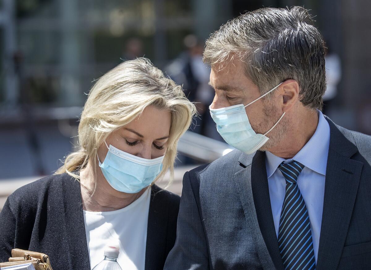A woman and a man wearing masks walk outside a courthouse