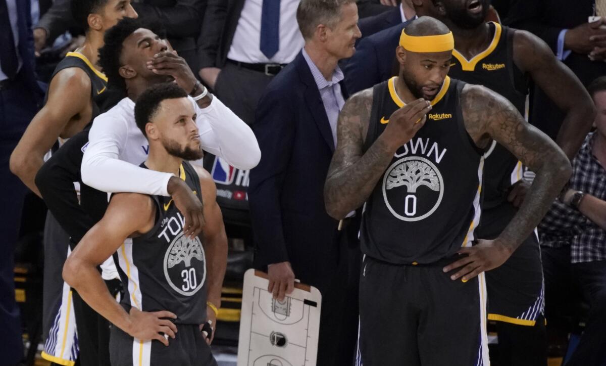 Golden State's Stephen Curry (30) watches with teammates Jordan Bell, left, and DeMarcus Cousins (0) as Toronto players celebrate their championship.