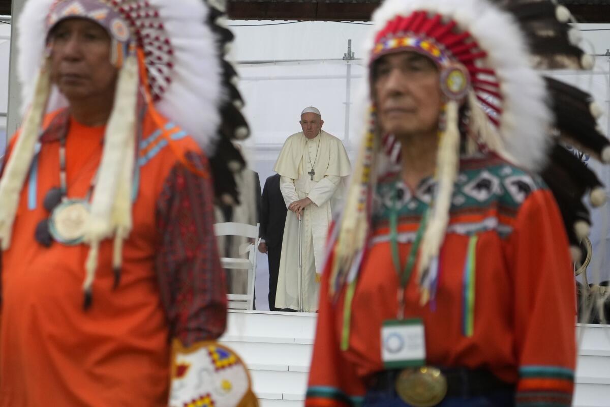 Men in Indigenous garb stand in the foreground as Pope Francis arrives for a meeting with Indigenous communities