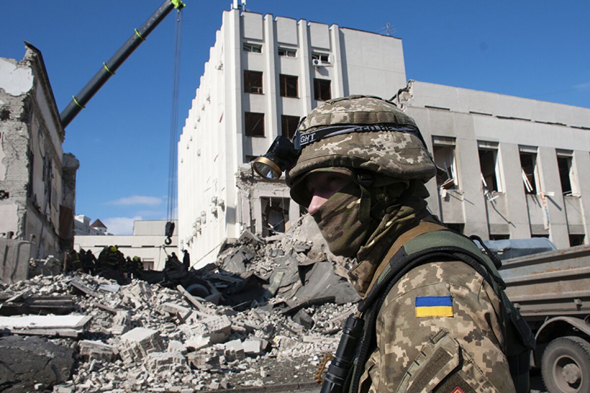 A Ukrainian soldier stands guard by a destroyed building.