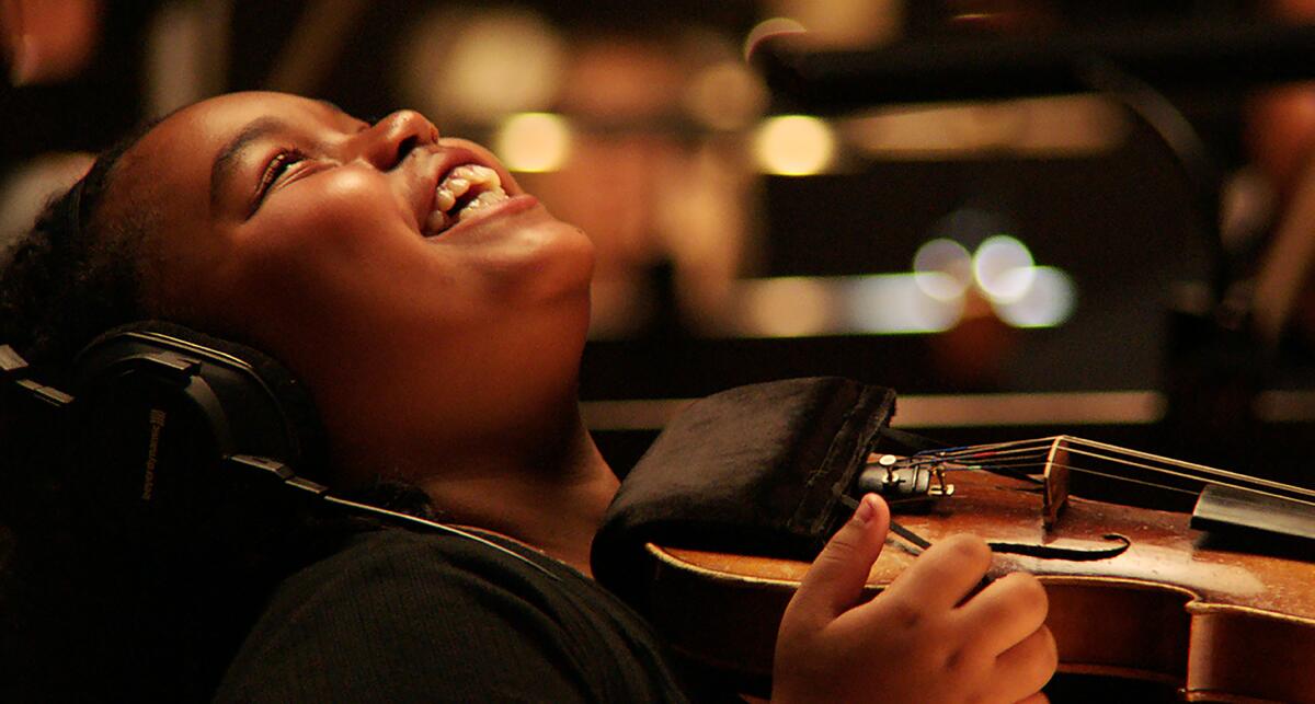 A girl reacts with a happy laugh as she holds a violin in "The Last Repair Shop."
