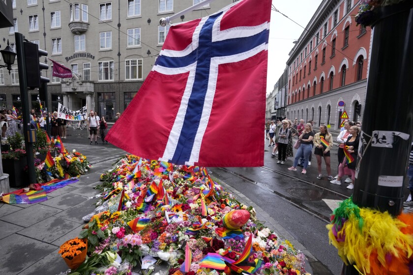 A Norwegian national flag flutters over flowers and rainbow flags that are placed at the scene of a shooting in central of Oslo, Norway, Sunday, June 26, 2022. Norwegian police say they are investigating an overnight shooting in Oslo that killed two people and injured more than a dozen as a case of possible terrorism. In a news conference Saturday, police officials said the man arrested after the shooting was a Norwegian citizen of Iranian origin who was previously known to police but not for major crimes. (AP Photo/Sergei Grits)