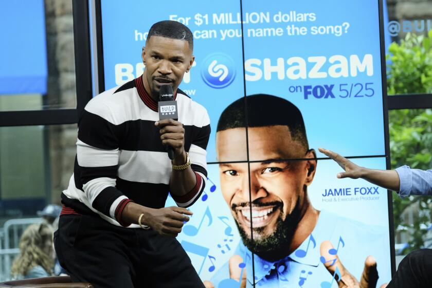 Actor Jamie Foxx speaks into a microphone in front of a promotional poster for his show 