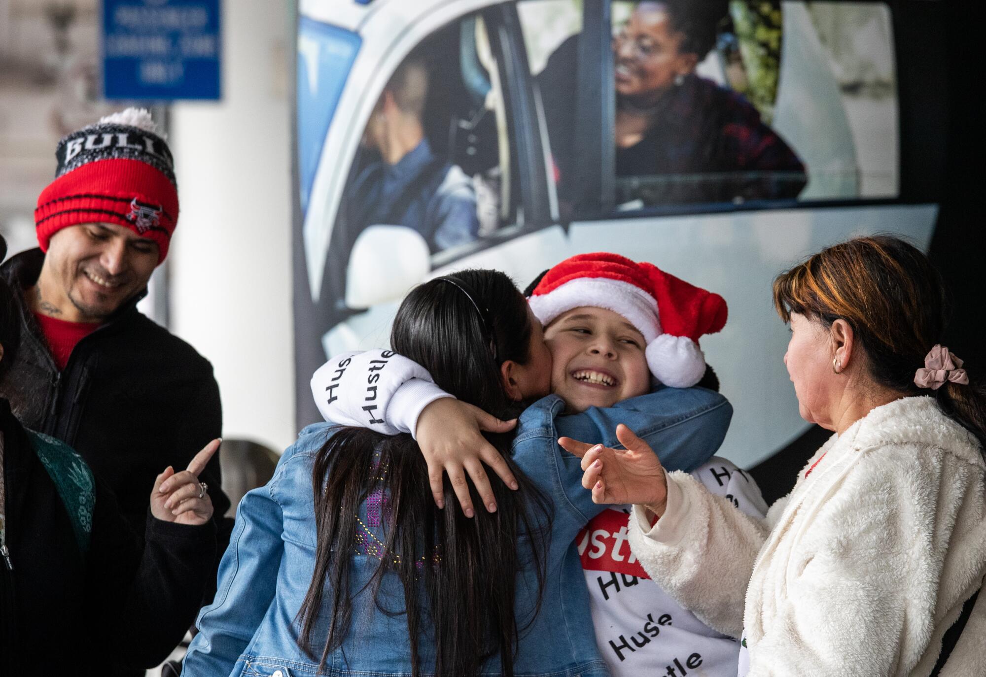An 11-year-old boy in a Santa hat embraces relatives at the airport.