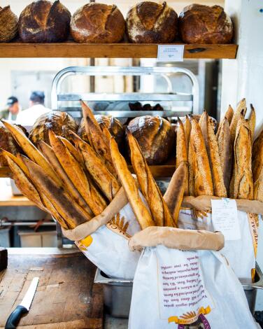 Baguettes in bags and boules on a shelf at Gjusta