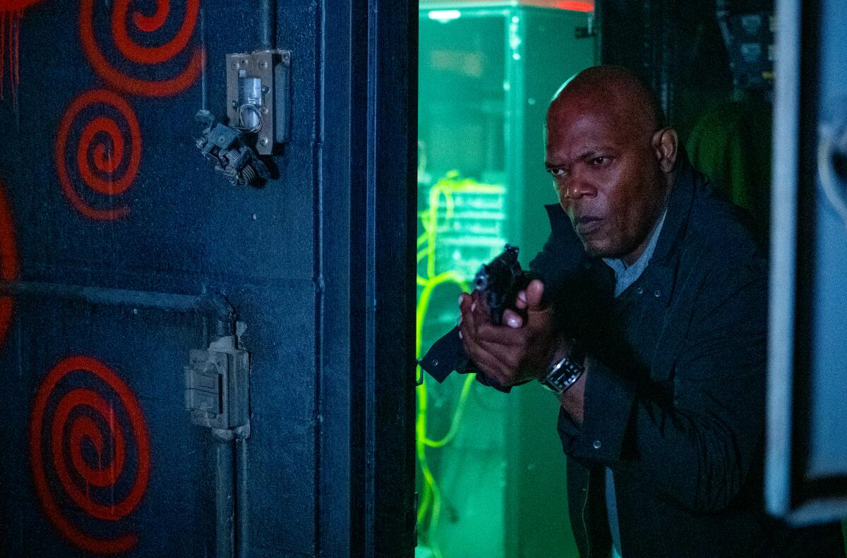 Samuel L. Jackson aims a gun into a room painted with spirals.