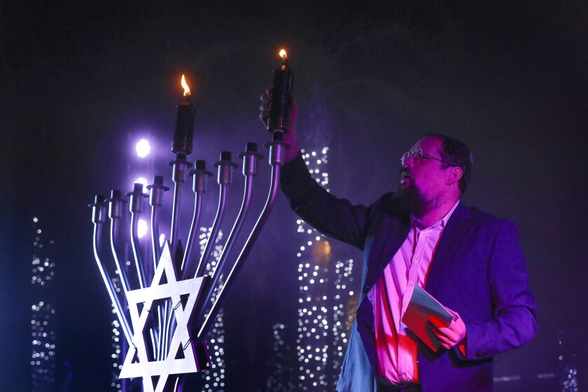 Rabbi Yossi Tiefenbrun of Chabad of Pacific Beach lights a candle in a menorah at Liberty Station.
