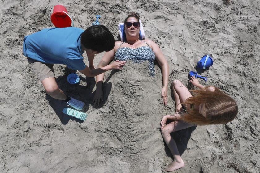Sophia Balangue gets covered with sand by her son Liam Balangue, 8, and her boyfriend's daughter Riley Sunblad, 7, as they spend a day at the beach on Friday March 27, 2020 in Oceanside, California.