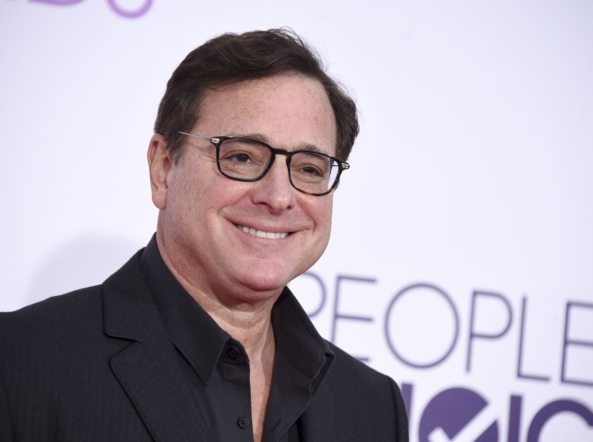 Bob Saget, in a black shirt and suit, smiles as he arrives at an awards show in Los Angeles.