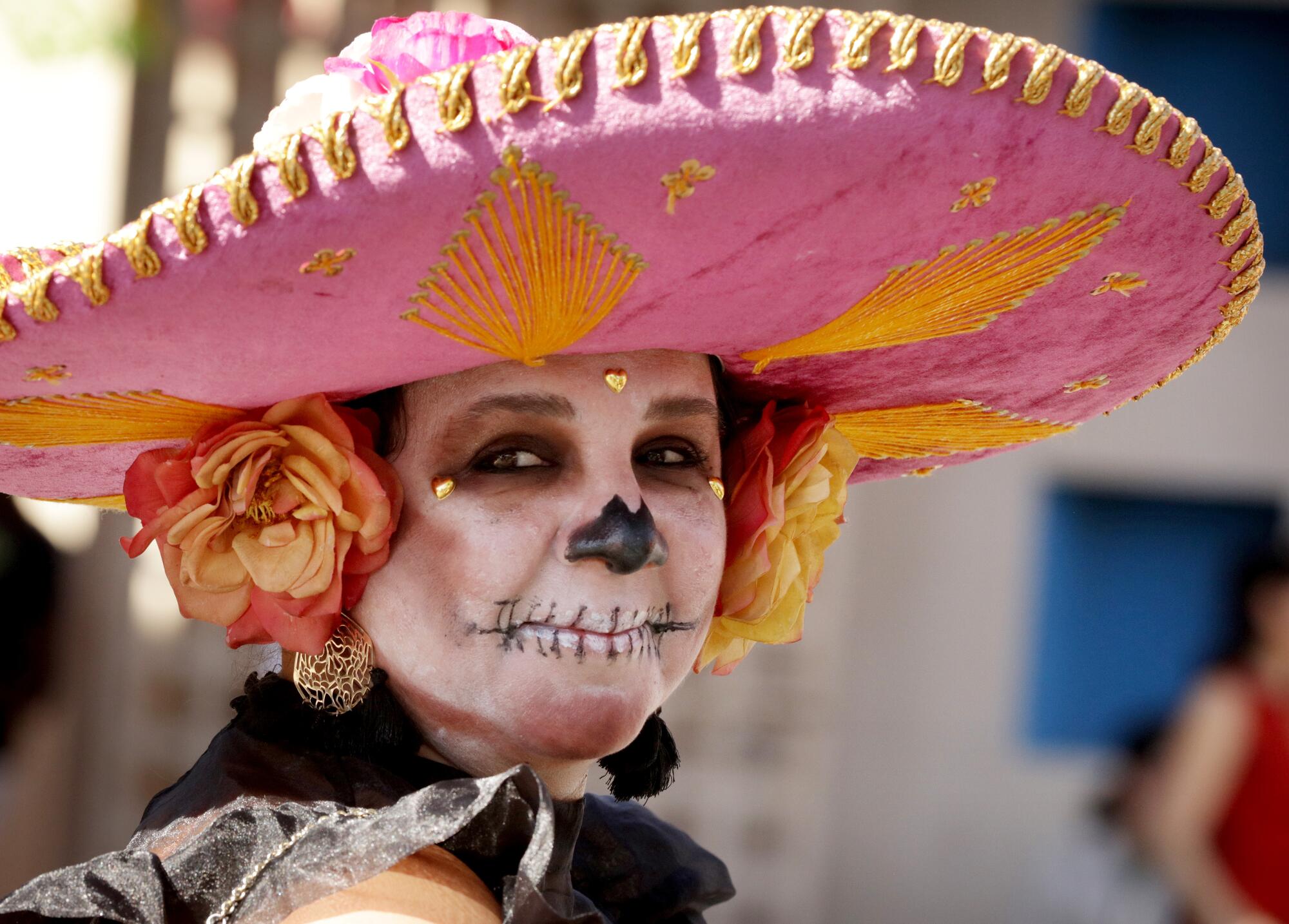 A woman in skul face paint and a pink sombrero outdoors.