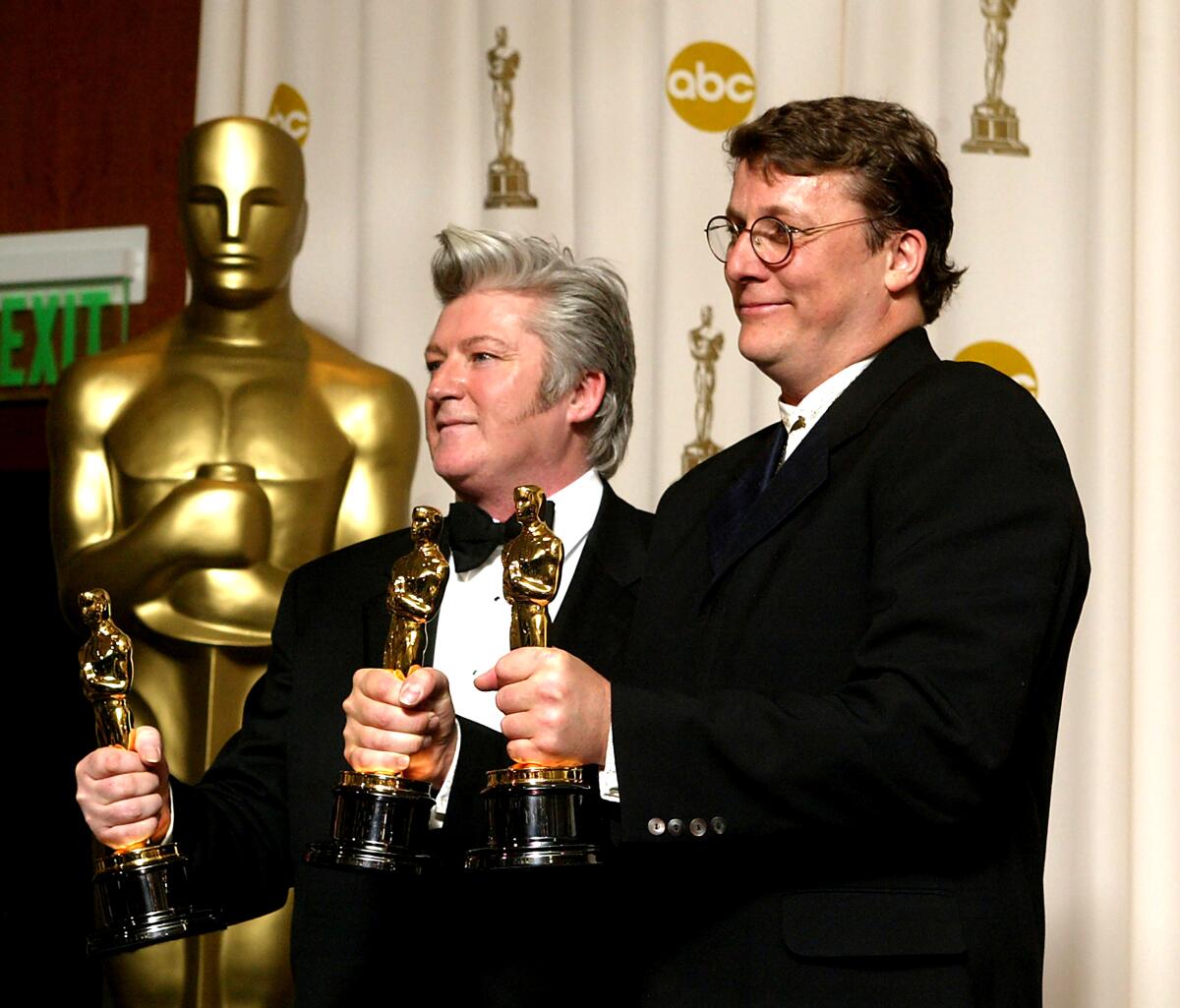 Two men stand backstage at the Academy Awards holding their Oscar statues.