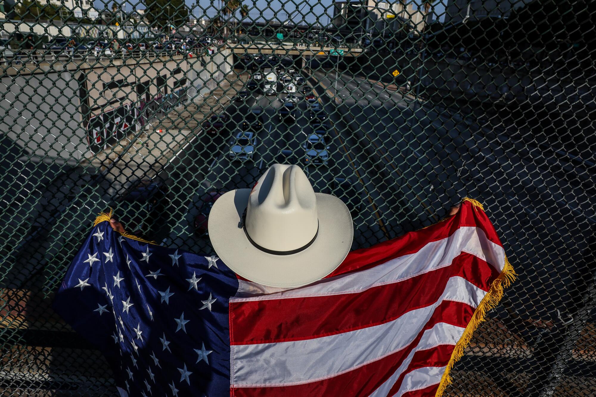 a man wearing a white cowboy hat looks out over a bridge with the American flag over his shoulders