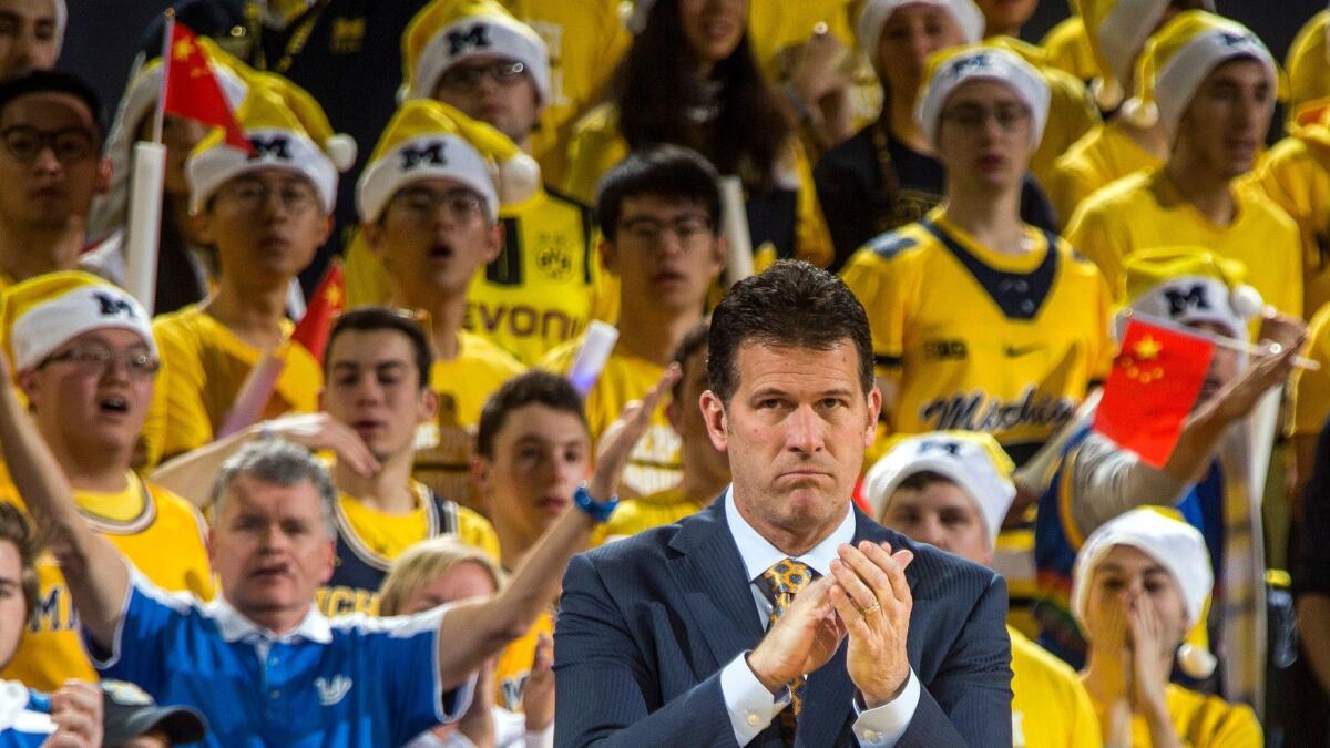 Michigan fans wave miniature Chinese flags behind UCLA coach Steve Alford during a Dec. 9 game.