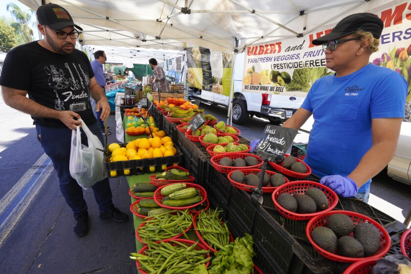 Sonny Sarzona from Gilbert and Lee Farms assists Kareem Captain with selecting vegetables at Little Italy farmers market.