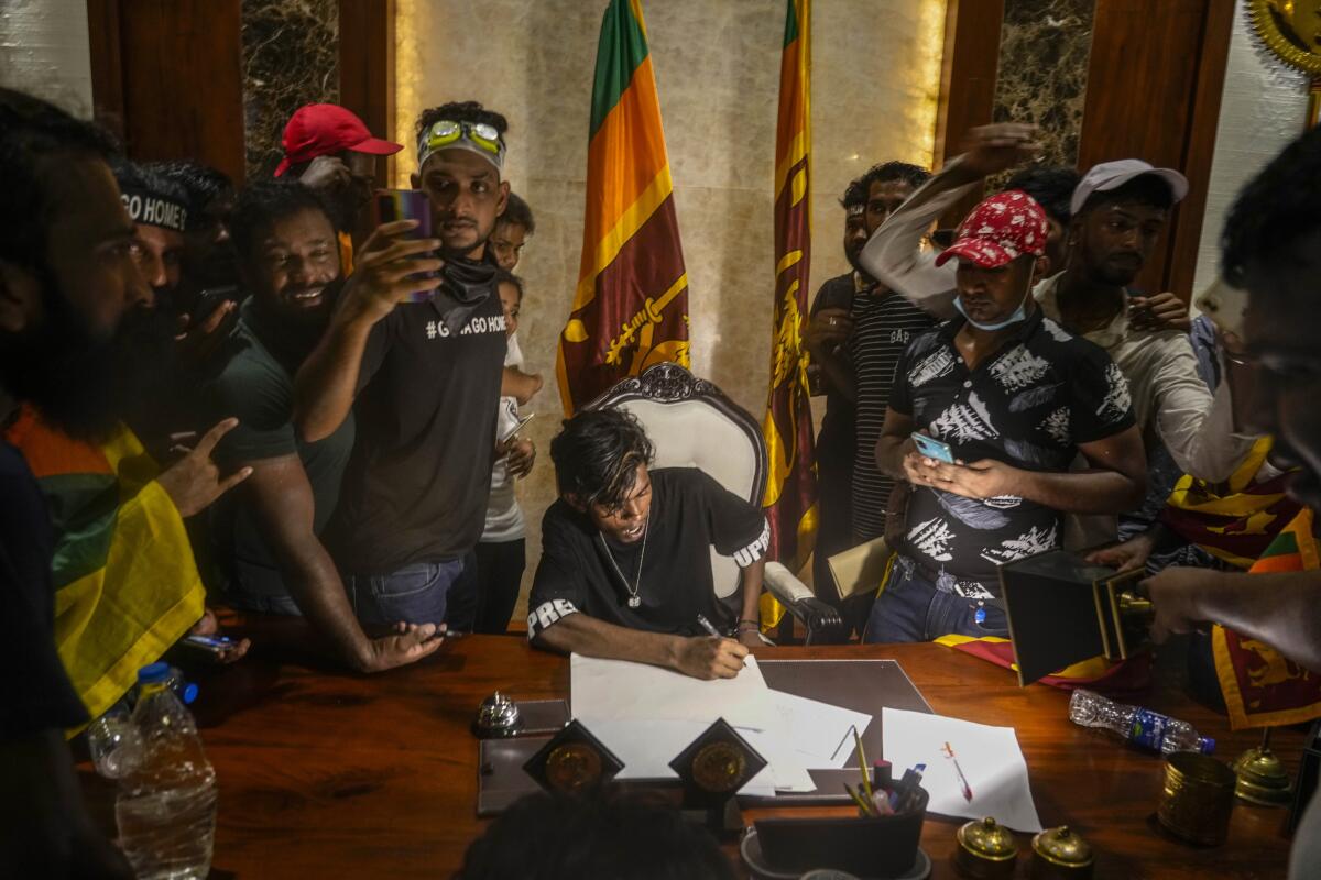 A protester sits on a chair surrounded by others after storming the Sri Lankan Prime Minister Ranil Wickremesinghe's office, demanding he resign after president Gotabaya Rajapaksa fled the country amid economic crisis in Colombo, Sri Lanka, Wednesday, July 13, 2022.(AP Photo/ Photo/Rafiq Maqbool)
