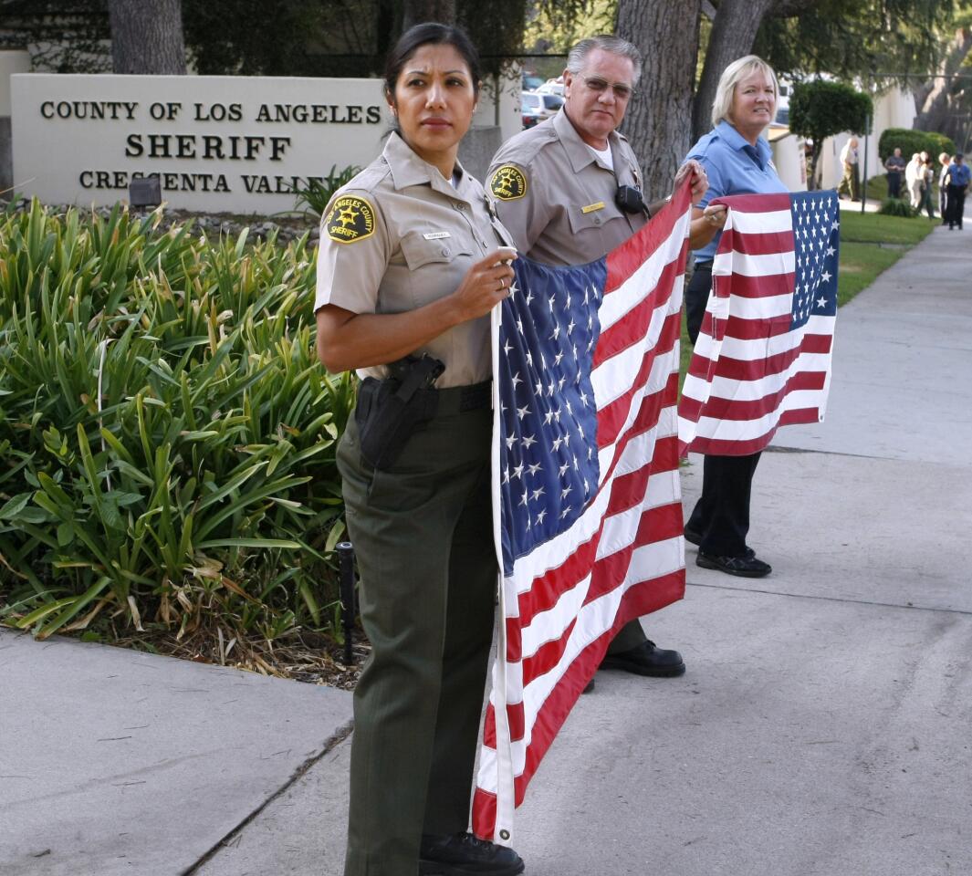 From left to right, L.A. County Sheriff Deputy Caroline Rodriguez, Deputy Randy Forney and law enforcement tech Deanna Hammerli wait for members of the Early Rodders Car Club to drive past the Crescenta Valley L.A. County Sheriff Station to honor heroes and victims of 9/11 in La Crescenta on Wednesday, Sept. 11, 2013. About 25 cars drove past local fire stations as well waving USA flags.