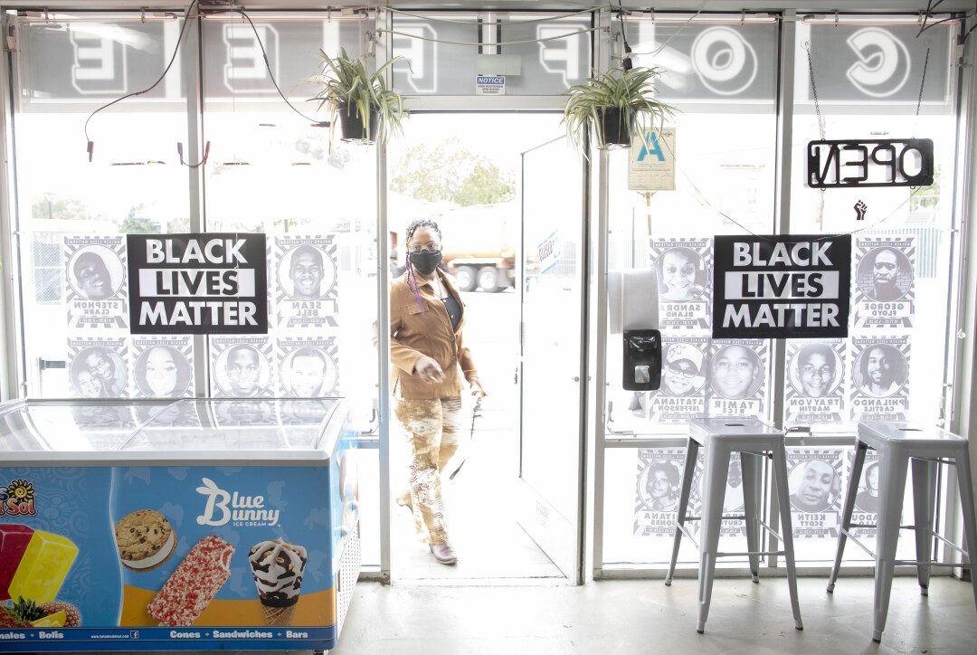 A woman walks through the door of a shop with Black Lives Matter signs in the window