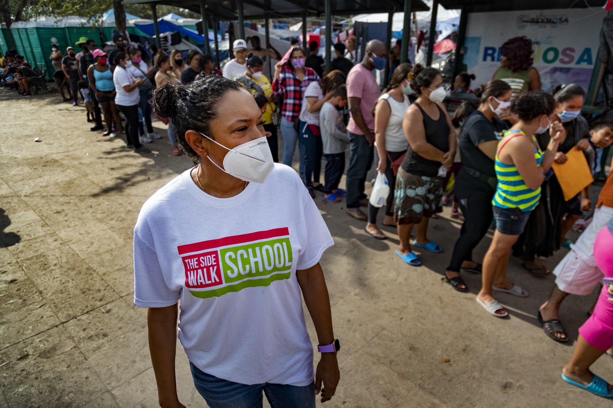 Activist Felicia Rangel-Samponaro walks along a line of migrants at a border camp clinic