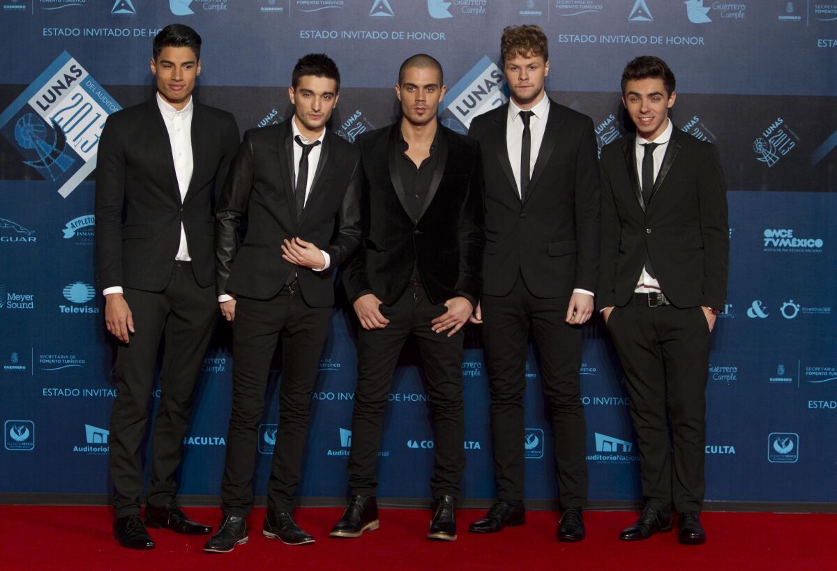 Five men in suits pose on a red carpet