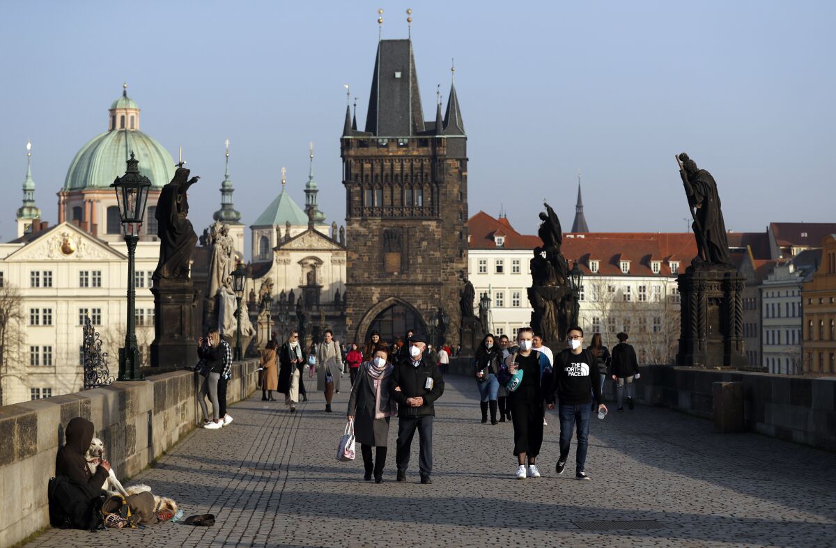 FILE - People wearing face masks walk across the medieval Charles Bridge in Prague, Czech Republic, on Feb. 25, 2021. The Czech Republic’s government has moved forward with easing coronavirus restrictions, cancelling a requirement for people to present a certificate proving they have been vaccinated or recovered from COVID-19 to be eligible to use various services and attend public events. People will no longer have to do it at bars, restaurants, cafes, hairdressers and others as well at sports and cultural events as of Thursday, Feb. 10, 2022. (AP Photo/Petr David Josek, File)