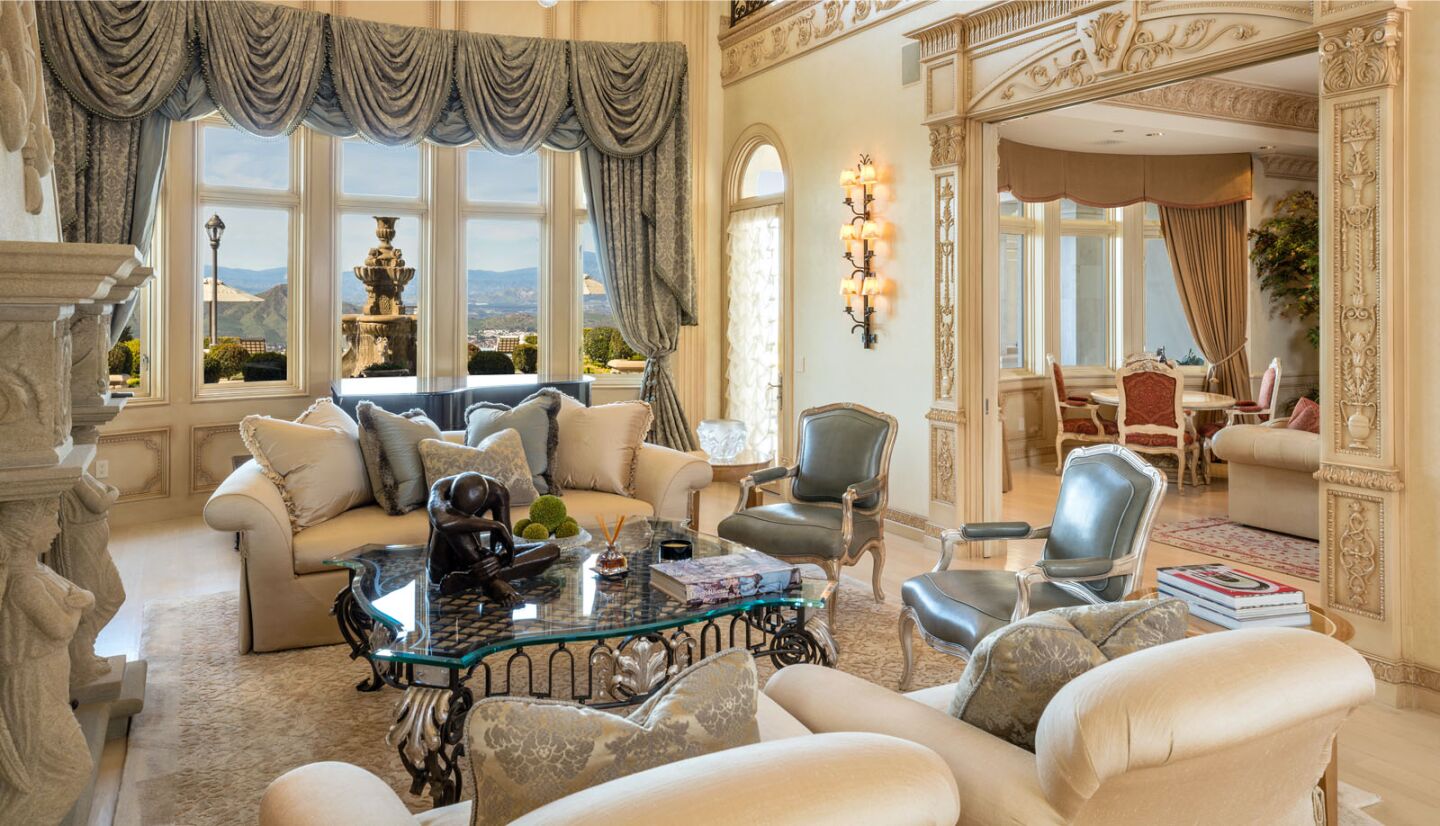 Elaborate draperies cover a window and a fireplace and doorframe feature sculptures and scrollwork.