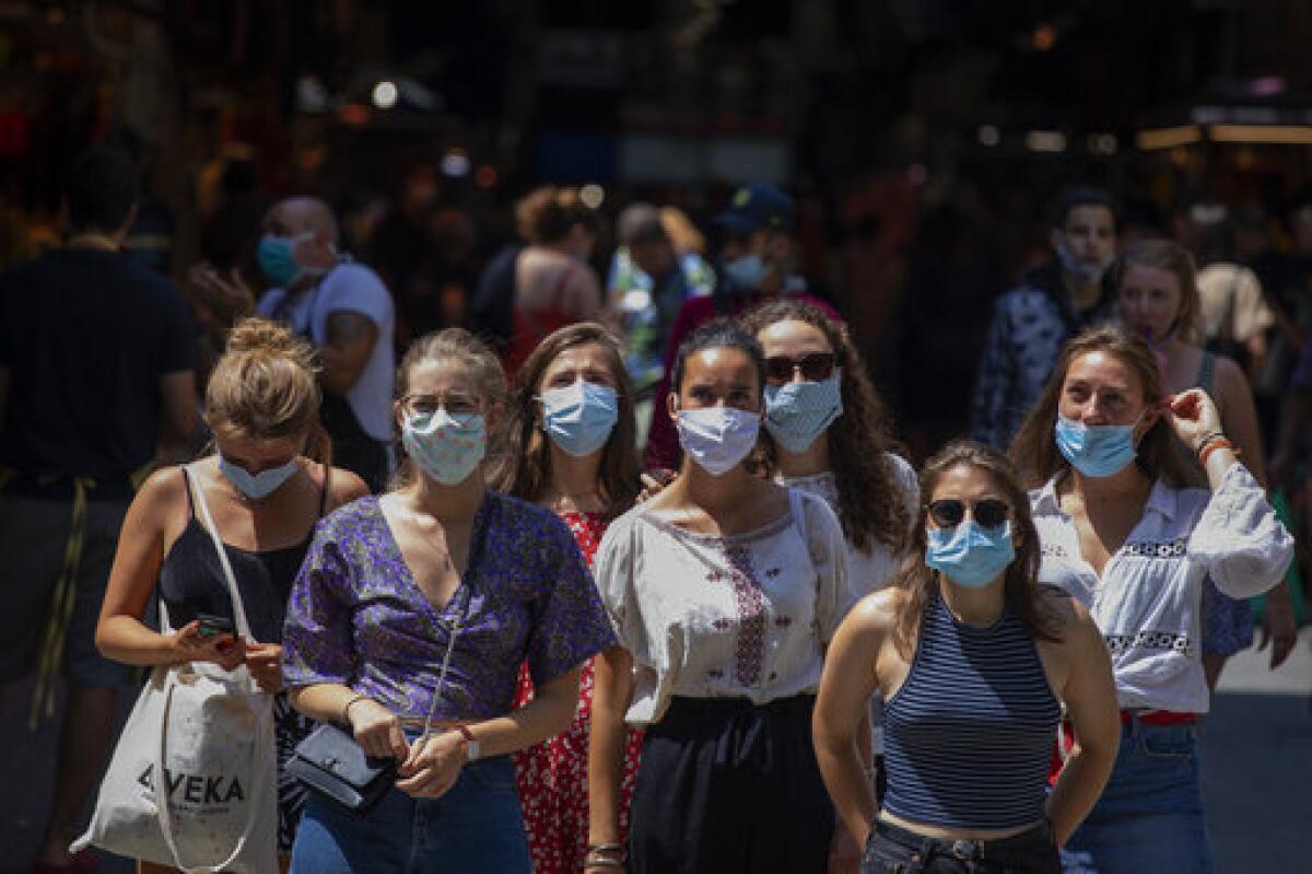 Tourists wearing face masks wait in downtown Barcelona, Spain.